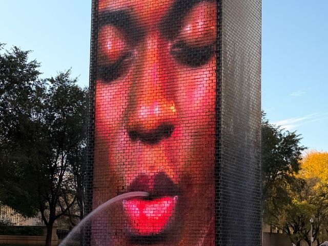 A giant face with closed eyes on a Crown Fountain tower, a stream of water spouting from its lips