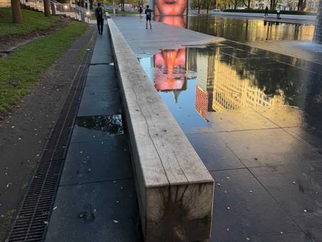 A long wooden bench beside the wet stone of Crown Fountain, a giant face reflected in the water
