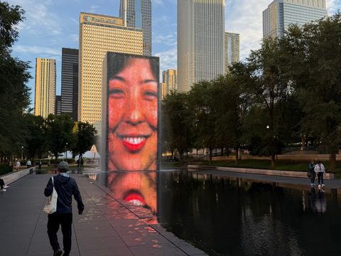 Crown Fountain in Millennium Park: a giant smiling face on a glass-brick tower glows above its reflecting pool, the Chicago skyline behind