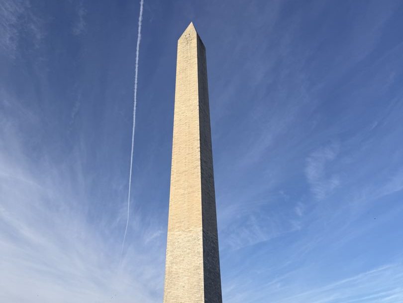 The Washington Monument against a blue sky crossed by a contrail